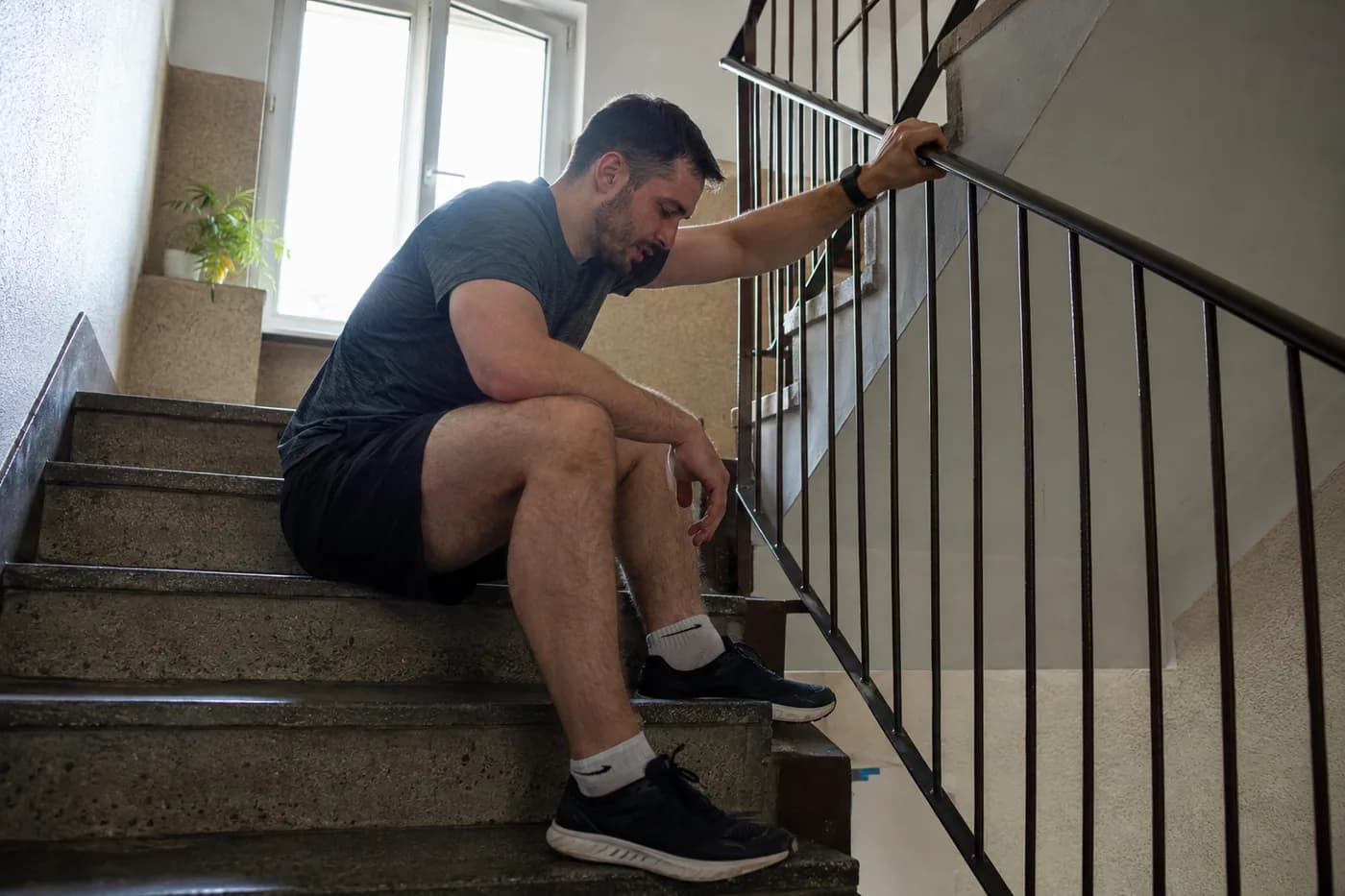 Mężczyzna siedzi na schodach po treningu, trzymając się poręczy