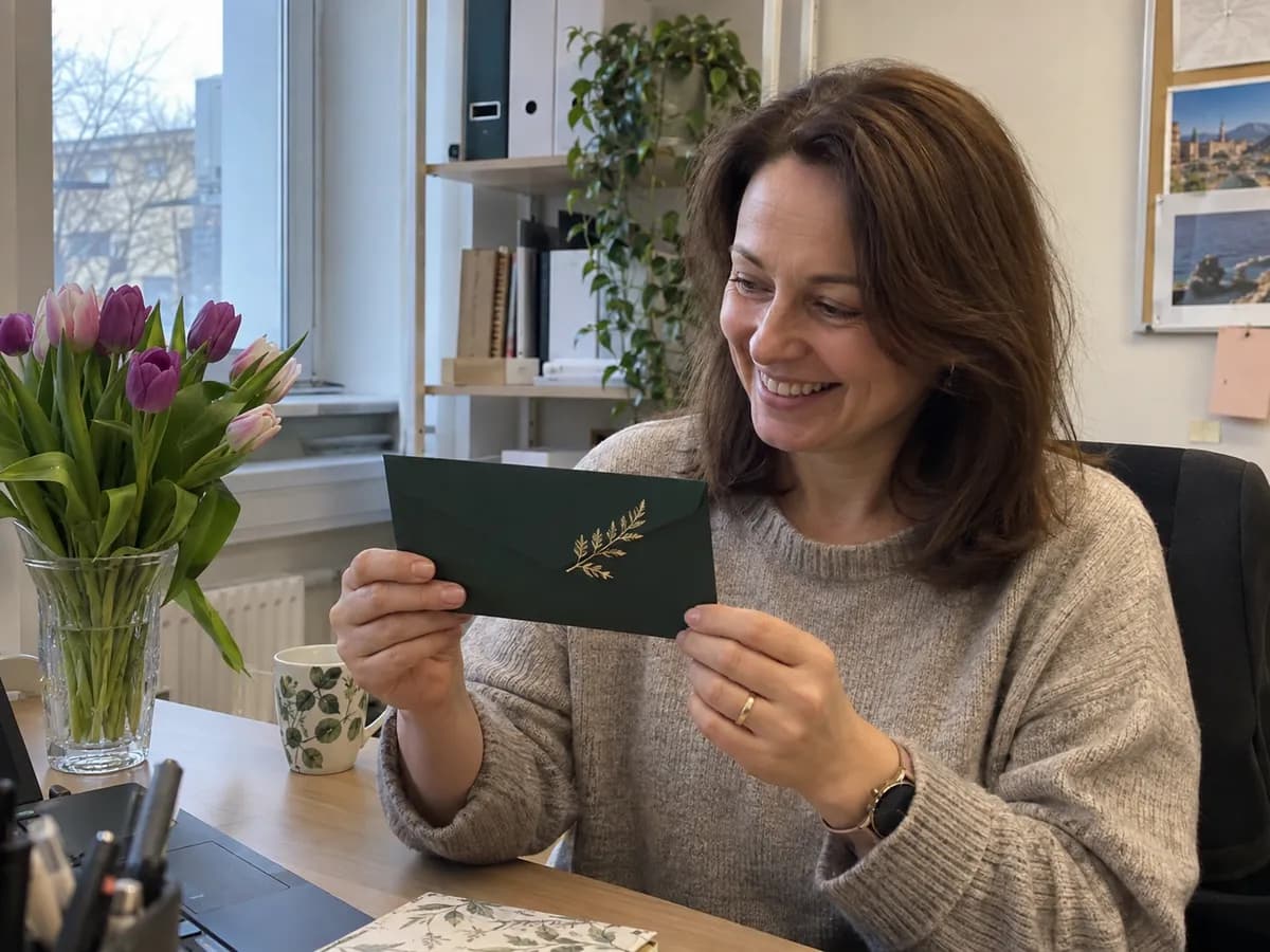 Kobieta przy biurku w jasnym biurze, trzyma voucher na masaż w zielonej kopercie i uśmiecha się